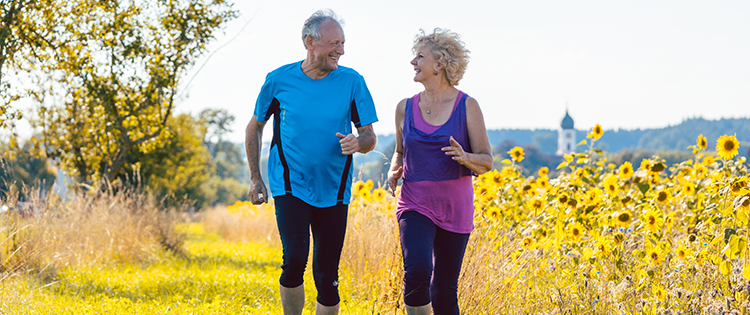 Senior man and woman running through a field of sunflowers. 