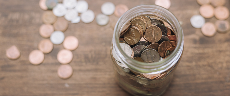 Glass jar filled with and surrounded by assorted coins with coins.