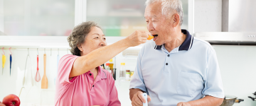 Senior couple cooking in the kitchen, woman feeding man.