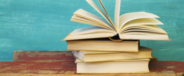 Stack of books on wooden table, with the top book open and pages flapping.