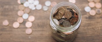 Glass jar filled with and surrounded by assorted coins with coins.