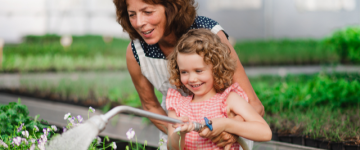 woman and young girl smiling and watering plants together.