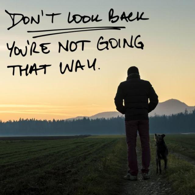 A man in a field walks towards the sunset with his dog. The text along the top reads "Don't look back. You're not going that way."